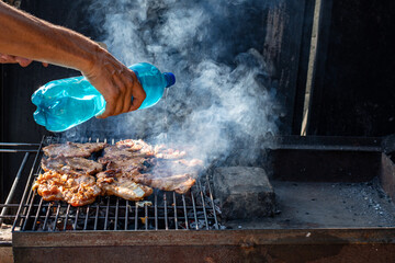 Man squirting water on hot charcoals while doing grilled chicken
