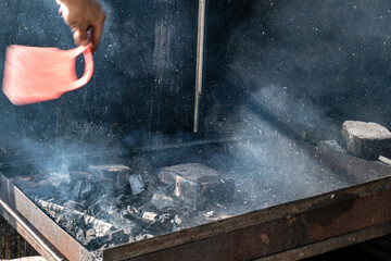 Man ventilating hot burned coals before grilling