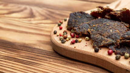 Cutting board with beef jerky and spices on wooden table. Close up.