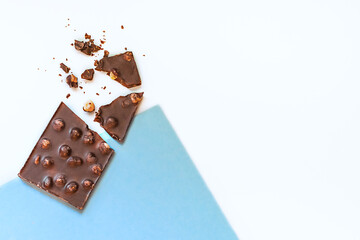 Composition of broken chocolate bar with nuts on a white and blue background. Top view. Copy space.