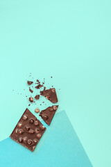 Composition from broken bars of chocolate with nuts on a blue background. View from above. Copy space.