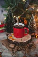 Cozy winter drink hot chocolate cocoa in red mug with fir tree, candles and Christmas lights.
