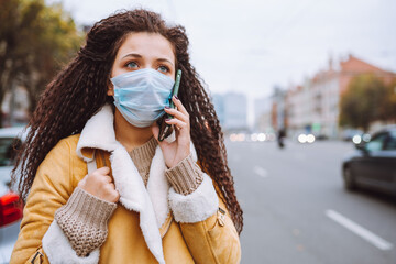 Beautiful afro haired woman wearing protective medical face mask stand on the street and talking by...