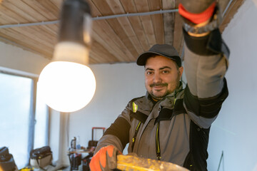 Fototapeta na wymiar smiling electrician plugged in a light bulb and admires the bright light that comes from it.