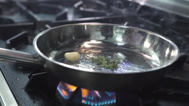 Frying fresh aromatic garlic clove and thyme twigs with oil in metal pan on modern stove with burning flame to cook delicacy food in kitchen extreme close view.