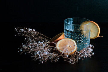 Alcohol drink (gin and tonic cocktail) garnished with lemon fruit and flower isolated on black background. Iced cocktail drink with lemon and herbs.