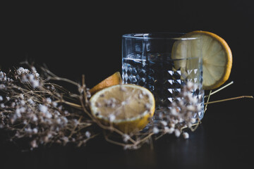 Alcohol drink (gin and tonic cocktail) garnished with lemon fruit and flower isolated on black background. Iced cocktail drink with lemon and herbs.