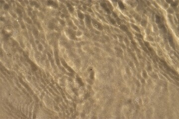 Ripples on the water, sea water near the coast, sand is visible through the water, top view