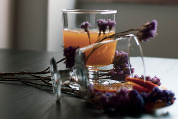 Glass of healthy Orange juice with pulp and sliced fruits isolate on wooden background with sunlight with purple flowers decorative. Orange juice and fresh fruits on table