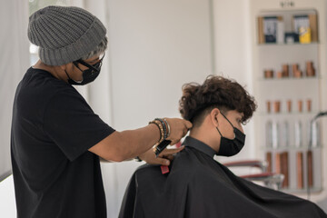 Session in a hair salon with a young hairdresser with a mask cutting the hair of a boy with a mask in times of pandemic