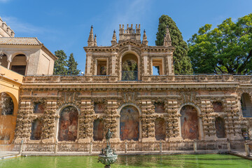 Naklejka premium The Fountain with the historical building with painting in the yard of the Real Alcazar Palaces in Seville