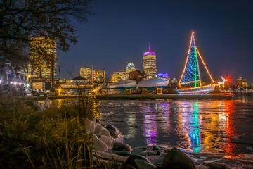 A sailboat decorated with Christmas lights on an icy Charles River
