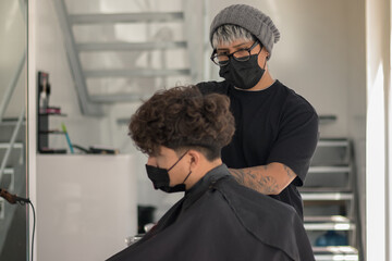 Session in a hair salon with a young hairdresser with a mask cutting the hair of a boy with a mask in times of pandemic