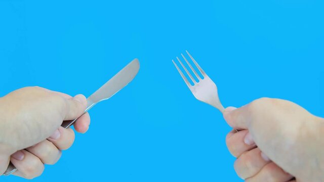 A person holding fork and knife against blue background, concept of a hungry man from a first person