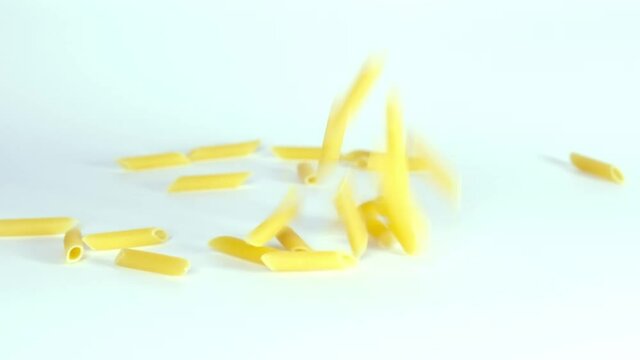 Raw uncooked penne pasta falling down in super slow motion against white background, slow mo