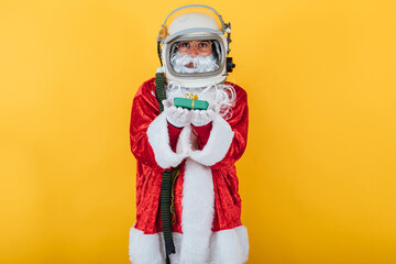 Fototapeta na wymiar Santa Claus with astronaut helmet holding a gift on yellow background. Christmas concept