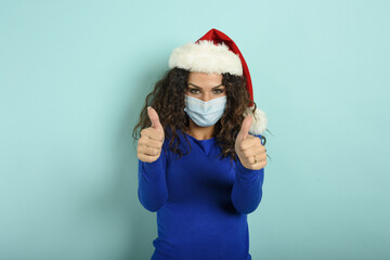 Fototapeta na wymiar Girl with christmas hat is optimistic about the defeat of covid 19 coronavirus. cyan background.
