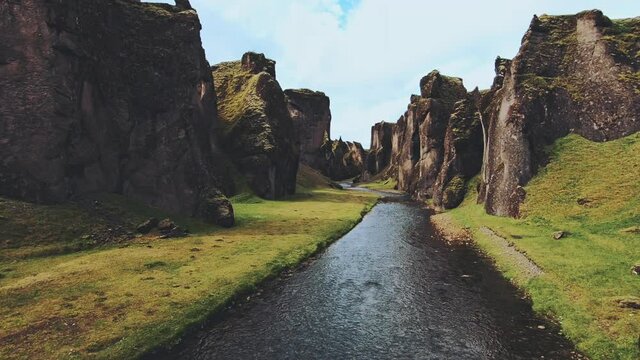 A slow drone shot flying through fjaðrárgljúfur canyon with moody greens and high contrast