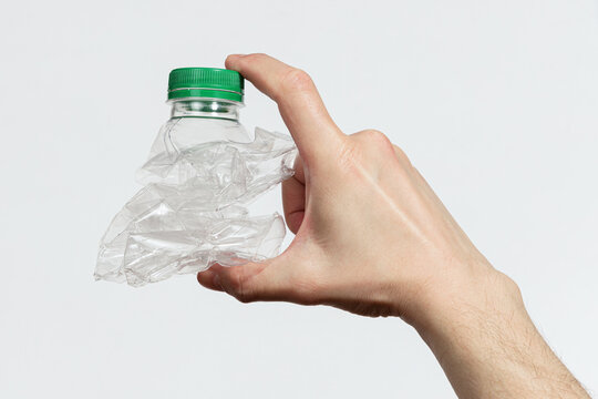 Hand holding smashed empty plastic bottle isolated on a white background