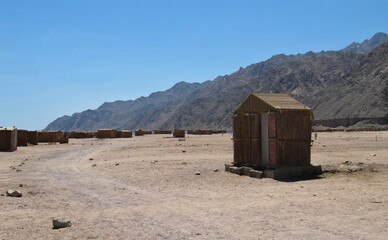 Lonely house and shacks near a dirt road against the backdrop of the Sinai Mountains. A gray ridge of mountains in a blue sky haze