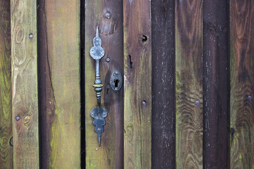 Old door lock and handle from metal in a weathered wooden wall, grunge background texture with copy space