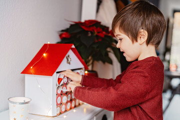 Little happy child opening first day in handmade advent calendar made from toilet paper rolls....