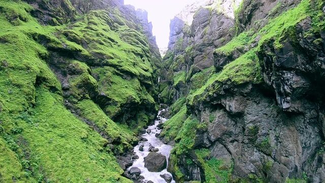 Slow shot of a green river canyon in Iceland with a small waterfall in the rocks