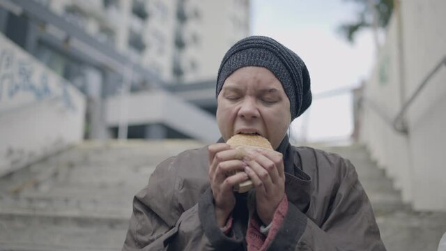 Hungry poor female eating fast food sandwich, basic needs of homeless person