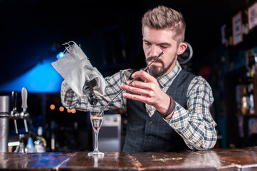 Bearded bartending pouring fresh alcoholic drink into the glasses while standing near the bar counter in nightclub