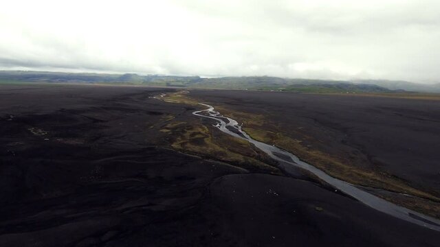 A drone shot of a winding river in Iceland with black sand, moss, and a foggy atmosphere