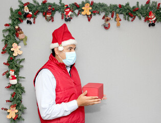 latin man with protection mask and gift box in christmas decoration, new normal covid-19