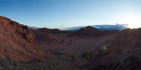 The red canyon and valley at sunset. Panorama view of the arid desert, sandstone formations, rocky mountains, lens flare and hiding sun in Talampaya national park in La Rioja, Argentina.