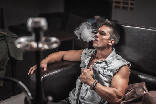 Sexy guy exhales smoke in hookah cafe.