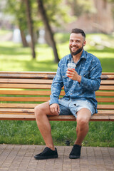 Fototapeta premium A guy with lemonade is resting in a park on a bench in the spring. Sunny day.