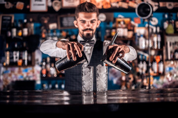 Young barman demonstrates the process of making a cocktail in the pub