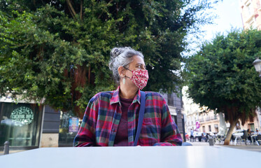 Caucasian female sitting in a cafe with a medical mask due to Covid-19 - the new normal concept