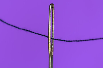 Closeup shot of a needle and thread on a purple background