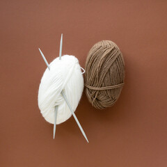 Knitting threads. Balls of beige and white yarn on a brown background, top view