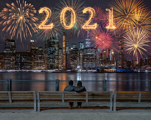 2021 written with Sparkle firework with multicolor of fireworks on back side couple sitting and...