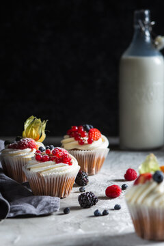 Homemade muffin next to a bottle of milk on a table and on a dark background with fresh berries around