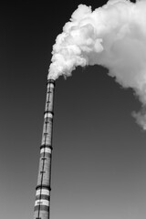 The thick smoke rises high from the industrial pipes. Pollution of the environment with waste products. Black and white photo.