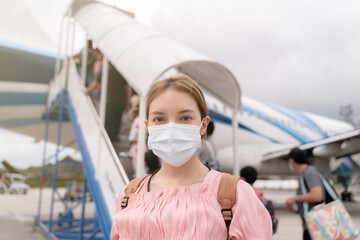 Fototapeta na wymiar Asian woman wearing protective face mask during covid-19 virus pandemic, walks to stair entering airplane, parking outside terminal in airport.