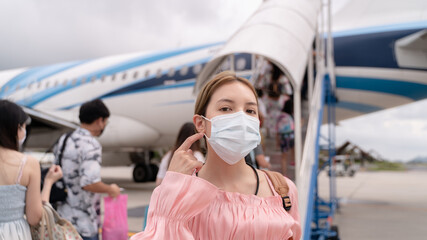 Asian woman wearing protective face mask during covid-19 virus pandemic,  walks to stair entering airplane, parking outside terminal in airport.