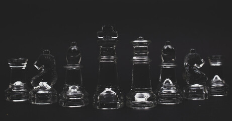 Obraz na płótnie Canvas lined up glass chess king, queen, bishop, knight and rock pieces on black background 