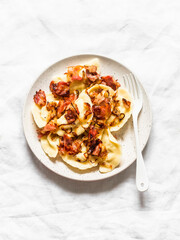 Potato pierogi with fried bacon and onions - delicious homemade lunch on a light background, top view