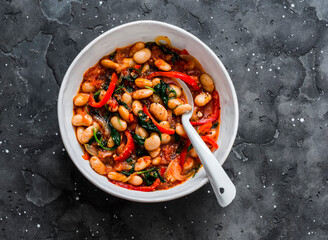 Greek style tomato sauce, spinach, paprika, beans stewed on a dark background, top view