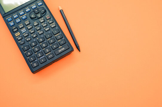 Top view closeup of a graphing calculator and a tiny pen isolated on an orange background