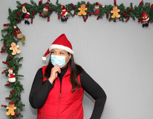 
Latin woman with protection mask, santa claus hat and red vest in Christmas decoration, new normal...