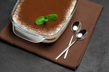 Traditional Italian Tiramisu dessert in glass baking dish on concrete background