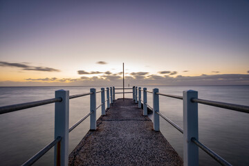 Fototapeta na wymiar Looking out over a pier against the ocean, a purple dusk horizon sky
